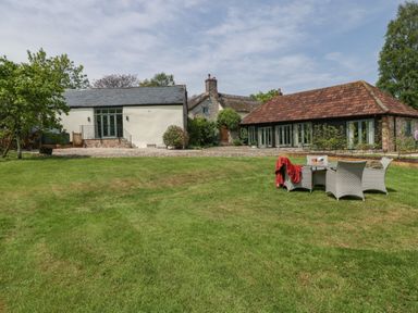 A grassy yard with outdoor furniture and three buildings in the background at The Hayloft in Stockland Honiton
