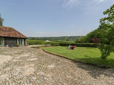A garden with a cobblestone driveway green lawn outdoor chairs and a table with an umbrella at The Hayloft in Stockland Honiton