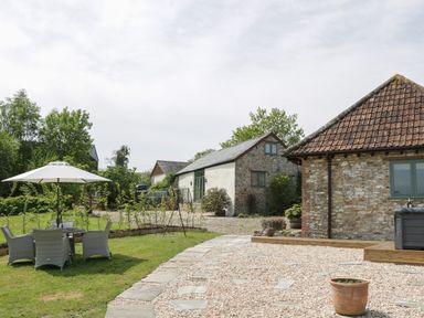 An outdoor garden area with a patio table and chairs under an umbrella next to stone buildings at The Hayloft in Stockland Honiton