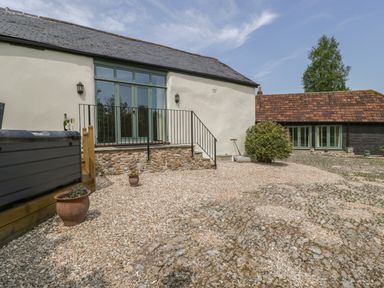 An outdoor area with gravel ground a hot tub and two buildings at The Hayloft in Stockland Honiton