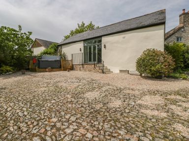 An outdoor area with a cobblestone and gravel ground next to a building with a gray slate roof and large windows at The Hayloft in Stockland Honiton