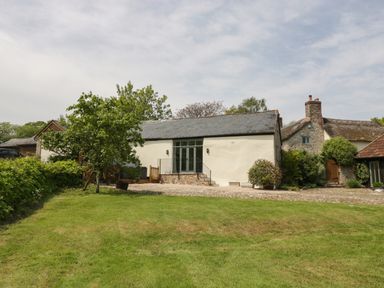 A grassy yard with a tree in front of a small building with a stone roof and cream walls at The Hayloft in Stockland Honiton