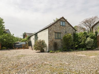 A stone cottage with a cobblestone driveway and greenery around the building at The Hayloft in Stockland Honiton