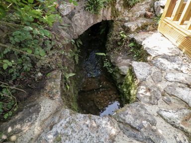 A small stone arch over a water channel with surrounding plants and stone paving at The Hayloft in Stockland Honiton