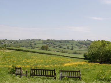 A field with three wooden benches overlooking rolling green hills at The Hayloft in Stockland Honiton