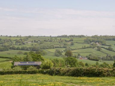 A rural landscape with green fields and trees and a barn with solar panels in the foreground at The Hayloft in Stockland Honiton