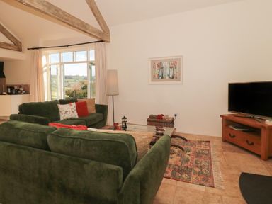A living room with green sofas a television on a wooden stand and a window with a view at The Hayloft in Stockland Honiton