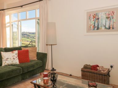 A living room with a green sofa pillows floor lamp wicker basket and glass coffee table at The Hayloft in Stockland Honiton