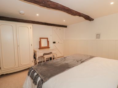 A bedroom with a bed, wardrobe, dressing table with mirror and wooden beams on the ceiling at The Hayloft in Stockland Honiton