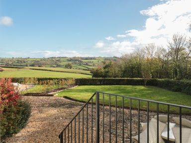 A garden with a lawn and patio furniture overlooking rolling green hills at The Hayloft in Stockland Honiton