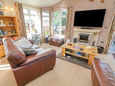 A living room with leather sofas a wooden coffee table a fireplace and a wall mounted TV at Mallard Lodge in Carnforth