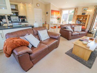 A living room with two brown leather sofas a wooden coffee table a bookshelf and a dining area with a table and chairs at Mallard Lodge in Carnforth