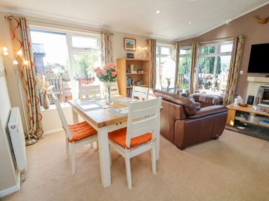 A dining table with four chairs and a vase of flowers next to a brown leather sofa in a living room at Mallard Lodge in Carnforth