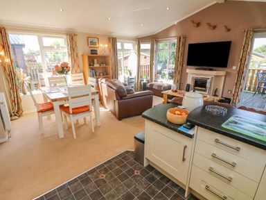 An open plan living area with dining table white chairs brown sofas fireplace and kitchen island at Mallard Lodge in Carnforth