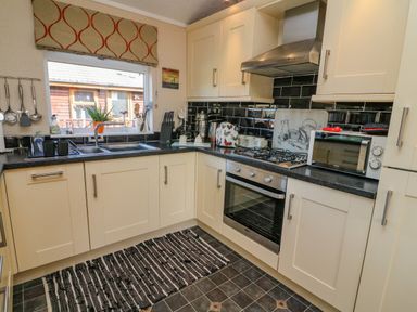 A kitchen with cream cabinets black countertops a stainless steel oven and range hood at Mallard Lodge in Carnforth