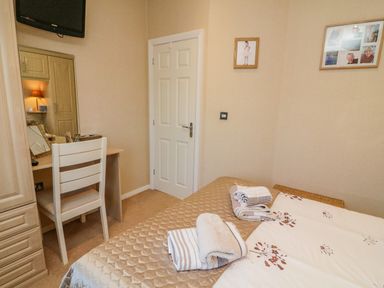 A bedroom with a bed holding folded towels a chair in front of a desk with a mirror and wall pictures at Mallard Lodge in Carnforth