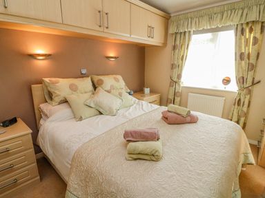 A bedroom with a bed with folded towels on it bedside tables and a window with curtains at Mallard Lodge in Carnforth