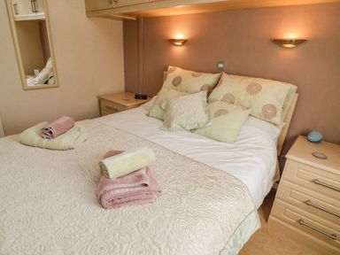 A bedroom with a bed with multiple pillows and folded towels on a quilt at Mallard Lodge in Carnforth