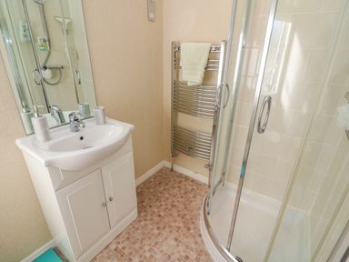 A bathroom with a white sink and cabinet a corner shower with glass doors and a chrome towel radiator with a towel at Mallard Lodge Carnforth