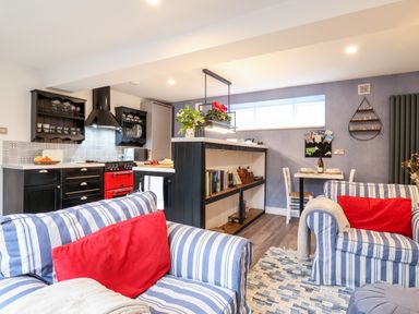 A kitchen and living room with striped sofas and red cushions at Tower End Cottage in Melton