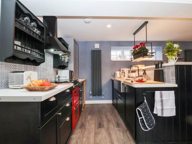 A kitchen with black cabinets white countertops and a red stove at Tower End Cottage in Melton