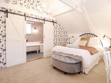A bedroom with a bed bedside tables lamps and an ottoman with sliding barn doors leading to a bathroom at Tower End Cottage in Melton