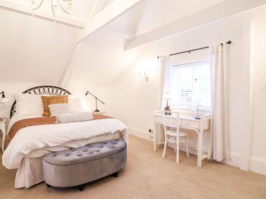 A bedroom with a bed a gray ottoman a white desk and chair under a window at Tower End Cottage in Melton