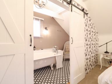 A bathroom with a clawfoot bathtub and patterned floor seen through sliding white doors at Tower End Cottage in Melton