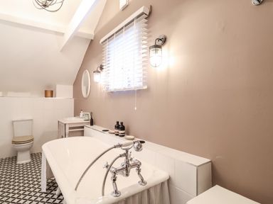 A bathroom with a bathtub sink toilet and window with blinds at Tower End Cottage in Melton