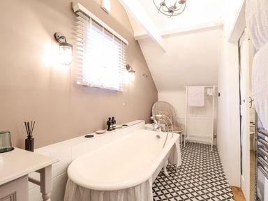 A bathroom with a clawfoot bathtub a wicker chair and patterned floor tiles at Tower End Cottage in Melton