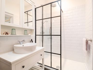 A bathroom with a white sink on a cabinet and a glass shower enclosure with black frames at Tower End Cottage in Melton