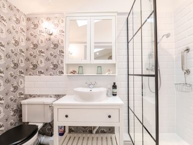 A bathroom with a white sink and vanity unit a toilet with black seat and a shower with glass partition at Tower End Cottage in Melton
