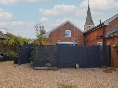 A courtyard with a gravel ground and a dark gate in front of a brick building with a church steeple in the background at Tower End Cottage in Melton