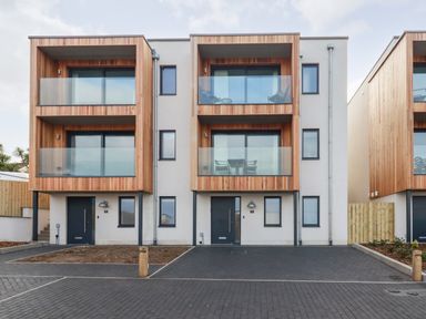 Modern two-story houses with wooden balconies and glass railings in front of paved driveways at Porth Beach Villa in Porth near Newquay