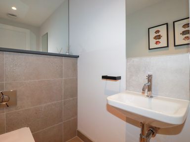 A bathroom with a wall-mounted sink and a toilet partially visible at Porth Beach Villa in Porth near Newquay