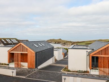A group of modern houses near the coast with grassy hills and ocean in the background at Porth Beach Villa in Porth near Newquay