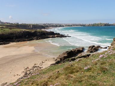A coastal landscape with a sandy beach rocky cliffs and ocean waves at Porth Beach Villa in Porth near Newquay