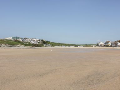 A wide sandy beach with buildings and grassy hills in the background at Porth Beach Villa in Porth near Newquay