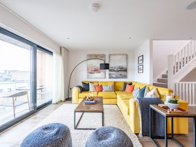 A living room with a yellow sectional sofa and a wooden coffee table at Porth Beach Villa in Porth near Newquay