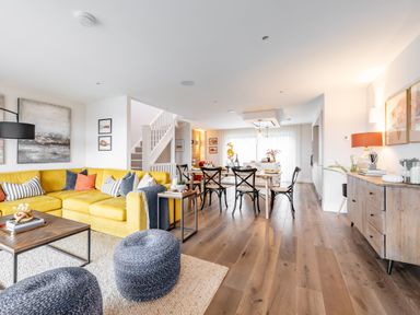 An open living and dining area with a yellow sofa, black chairs, wooden table, and staircase at Porth Beach Villa in Porth near Newquay