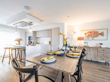 A dining area with a wooden table set for six and a kitchen with an island and stools at Porth Beach Villa in Porth near Newquay