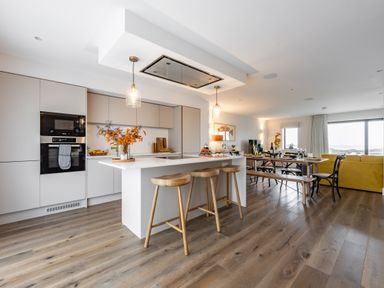 A kitchen with an island and wooden stools next to a dining table and yellow sofa at Porth Beach Villa in Porth near Newquay