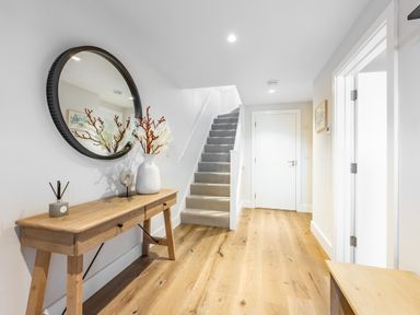 A hallway with a wooden console table a round mirror and stairs at Porth Beach Villa in Porth near Newquay