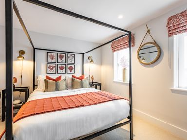 A bedroom with a black four-poster bed white linens orange throw pillows and wall art at Porth Beach Villa in Porth near Newquay