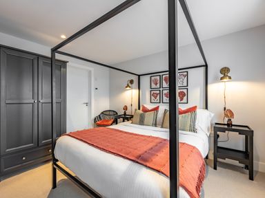 A bedroom with a black four poster bed covered with white bedding and red throws near black side tables and a black wardrobe at Porth Beach Villa in Porth near Newquay