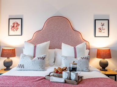 A bedroom with a bed with pillows bedside lamps and framed pictures on the wall at Porth Beach Villa in Porth near Newquay