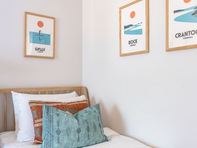 A bed with patterned cushions and three framed prints on the wall above at Porth Beach Villa in Porth near Newquay
