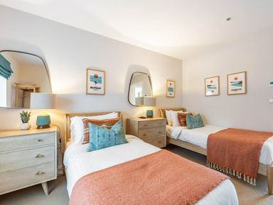 A bedroom with two single beds each with pillows and orange blankets with wooden dressers and wall mirrors at Porth Beach Villa in Porth near Newquay