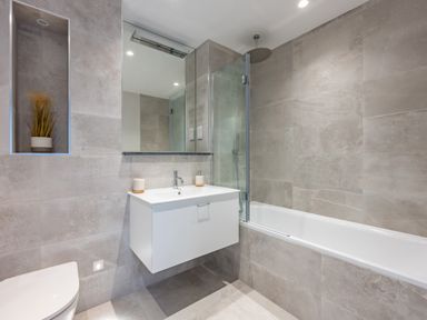 A bathroom with a bathtub a wall-mounted sink a mirror and a built-in niche with a plant at Porth Beach Villa in Porth near Newquay