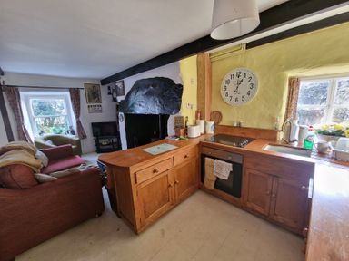 A kitchen with wooden cabinets and an oven next to a living area with sofas and a TV at Quarry Cottage in Blaenau Ffestiniog